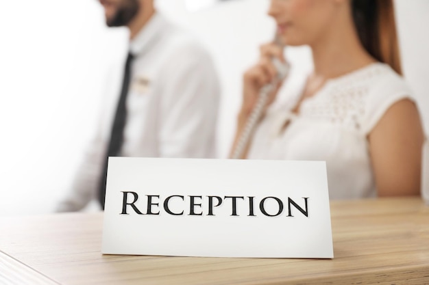 Foto cartello della reception e due occupati lavoratori dell'hotel sullo sfondo