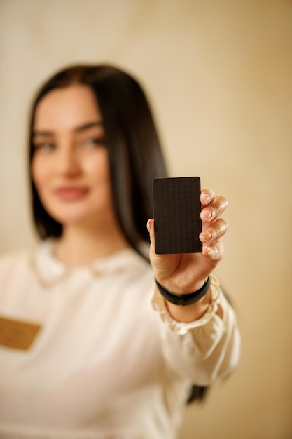 Receptionist girl with visit card in hands close up the hostess\
at the reception holds a business card of the company or hotel\
place for your logo