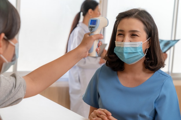 Receptionist e ospite che indossa la maschera per il viso alla reception mentre conversano in ufficio o in ospedale