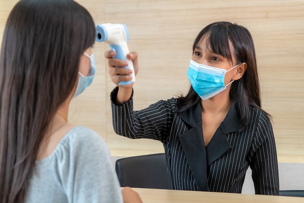 Receptionist and guest wearing face mask at front desk while having conversation in office or hospital