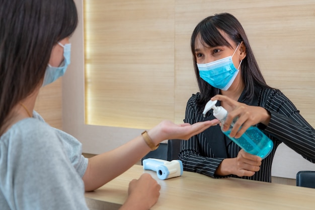 Receptionist and guest wearing face mask at front desk while having conversation in office or hospital