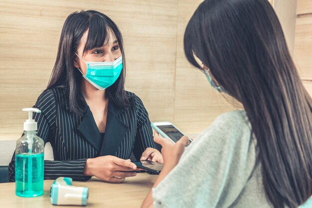 Receptionist and guest wearing face mask at front desk .