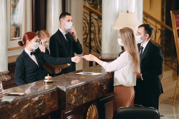 receptioniste aan balie in hotel met medische maskers