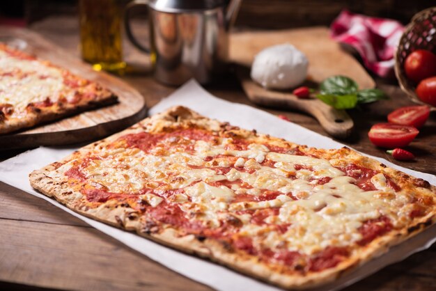 Rechthoekige zelfgemaakte pizza op rustieke tafel met mozarella tomaat en basilicum close-up