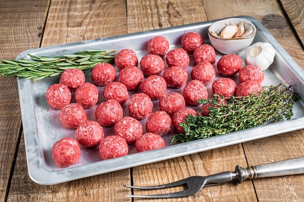 Recipe for cooking meatballs from ground beef with thyme and rosemary in kitchen tray. Wooden background. Top view.