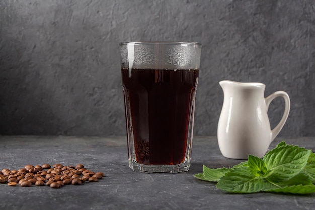 Recipe Ice coffee with mint and milk. Large glass with black coffee. Cool summer drink on dark background in low key. Close up, copy space for text.