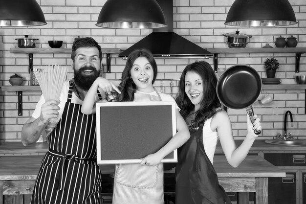 Recipe of perfect family dinner Mother and father with little girl holding chalkboard copy space Little girl with parents cooking Family day Happy family in kitchen Pleasant time together