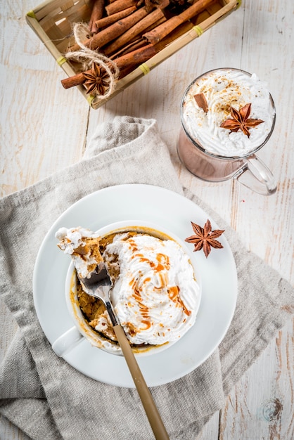 Recipes with pumpkins, fast food, microwave meal. Spicy pumpkin pie in mug, with whipped cream, ice cream, cinnamon, anise. On white wooden table, with cup of hot chocolate. copyspace top view
