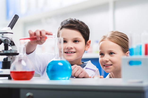 Foto comportamento avventato. bambini allegri allegri e allegri che fissano i bicchieri da laboratorio mentre sorridono e conducono esperimenti