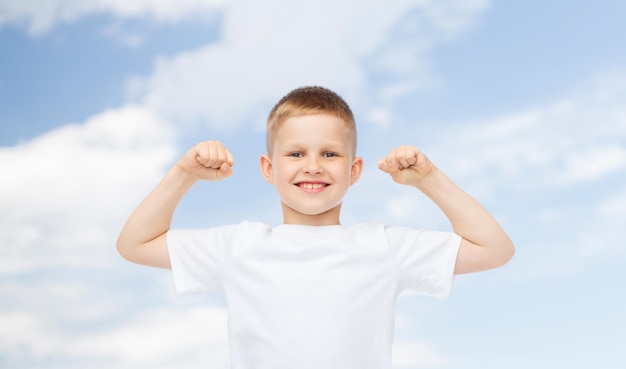 reclame, ecologie, mensen en jeugdconcept - glimlachend jongetje in wit leeg t-shirt dat biceps buigt over blauwe hemelachtergrond