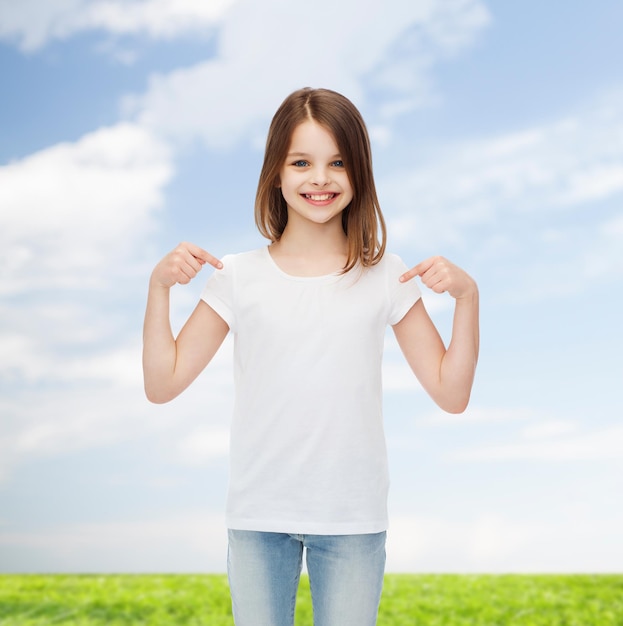 reclame, jeugd, gebaar en mensen concept - glimlachend meisje in wit t-shirt wijzende vingers op zichzelf over natuurlijke achtergrond