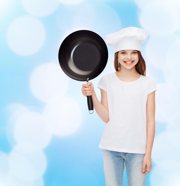 reclame, jeugd, koken en mensen - lachend meisje in wit t-shirt en kookhoed met pan op blauwe achtergrond