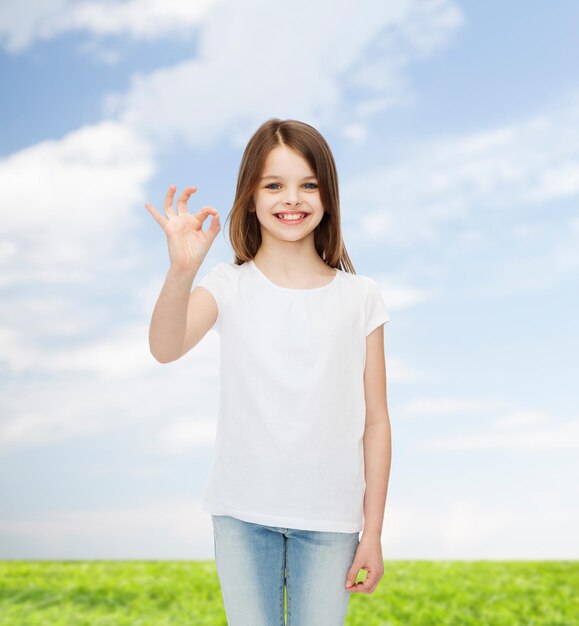 reclame, jeugd, zomer, gebaar en mensenconcept - glimlachend meisje in wit leeg t-shirt met ok teken over natuurlijke achtergrond