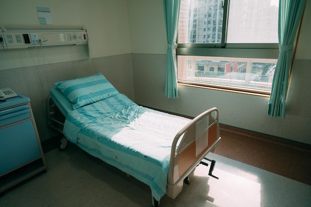 침대와 편안한 의료가 있는 회복실. 실내 창문을 통해 햇빛이 비치는 빈 병실 내부. 클리닉 개념의 병동에 의료 장비가 있는 평화로운 장소.