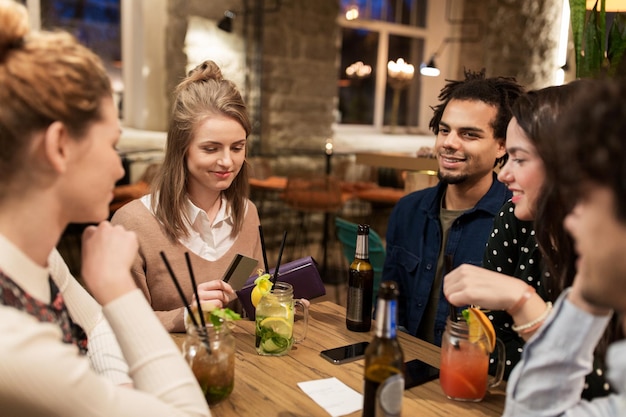 recreatie, mensen en vakantie concept - gelukkige vrienden met dranken, creditcard en rekening in de bar of café