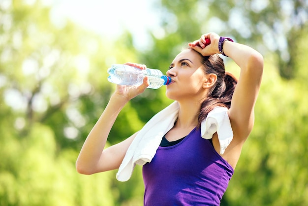 Recreation of young sporty woman with with arm raised on the head and drinking water on nature park forest background Sport Pause