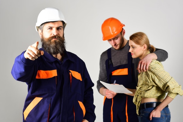 Recruitment concept Brigade of workers builders in helmets repairers and lady discussing contract grey background Brigadier hiring workers for repair sign contract Bearded man points forward