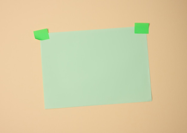 Rectangular blank green sheet of paper glued with green sticky paper on light brown background, copy space