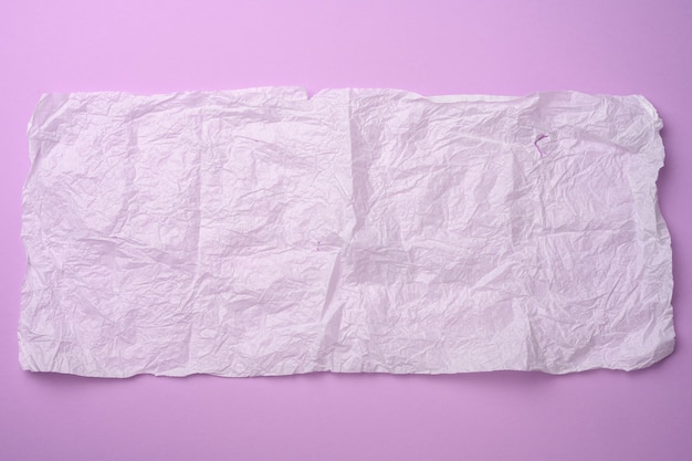 Rectangular crumpled sheet of paper in tissue on a purple surface, copy space