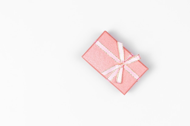 Rectangular gift box of pink pastel color with ribbon and bow close-up against a white background with natural shadow, top view, copy space