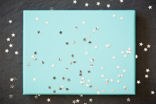 Прямоугольная голубая или бирюзовая коробка на черном фоне с украшениями из серебряных звезд