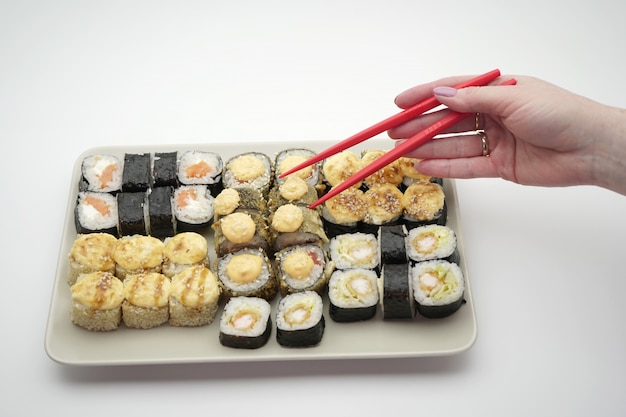 Rectangular plate full of sushi rolls and sticks of red color, on an isolated background, close-up