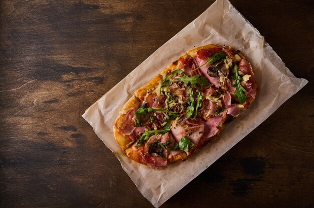 Rectangular roman pizza with prosciutto ham tomatoes mozzarella\
mushrooms and arugula on wooden