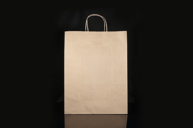 黒い背景にモックアップされた、購入ギフトや持ち帰り用の食品用のリサイクル可能なクラフト紙袋 使い捨てのビニール袋よりも環境に優しい