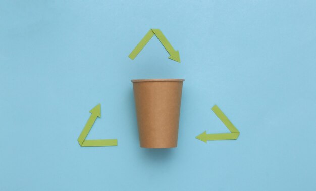 Recycled arrows sign and coffee cup on blue background. Eco concept. Top view