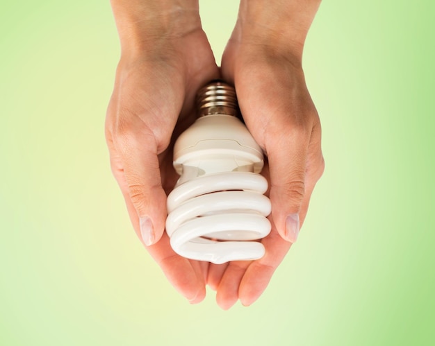 Photo recycling, electricity, environment and ecology concept - close up of hands holding energy saving lightbulb or lamp over green background