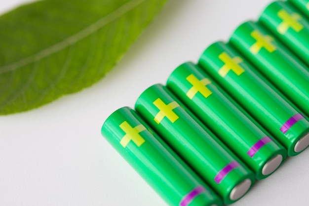 recycling, energy, power, environment and ecology concept - close up of green alkaline batteries and leaf