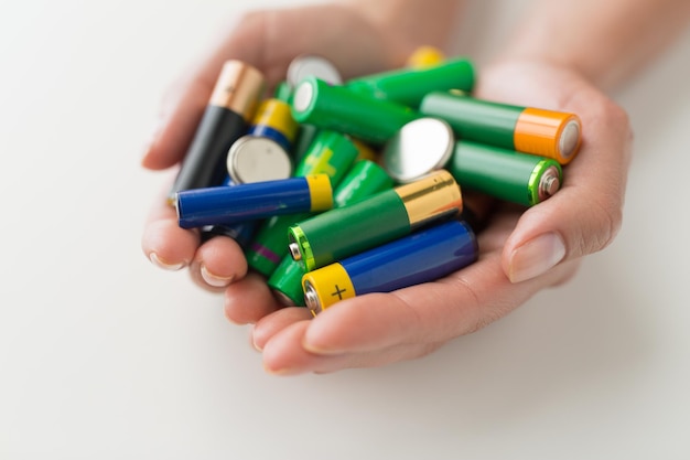 recycling, energy, power, environment and ecology concept - close up of hands holding alkaline batteries heap