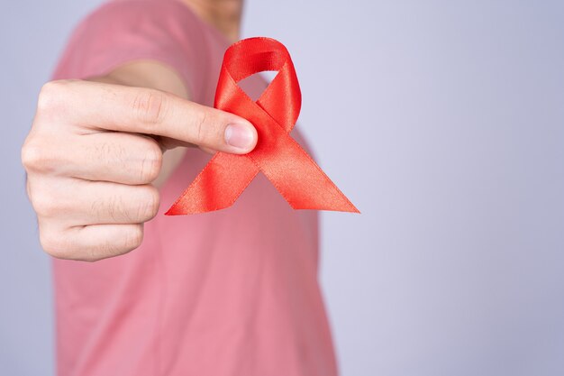 Red AIDS awareness ribbon holding by man on grey