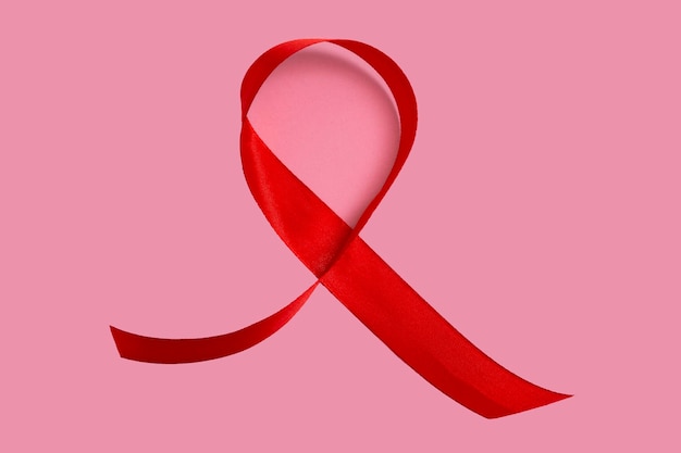 Red AIDS awareness ribbon on pink background. Close up, copy space.