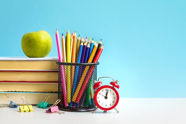 Red alarm clock, apple, color pencils, books on blue 