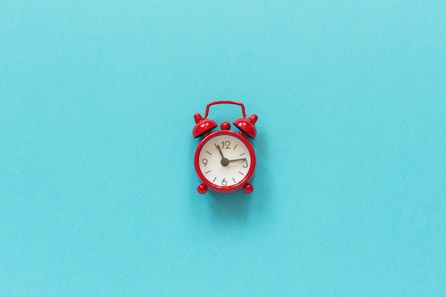 Red alarm clock in center on blue paper background. 