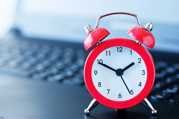 Red alarm clock on a computer keyboard, with a blurred background and a shallow depth of field.