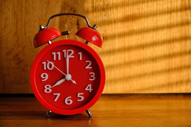 Red alarm clock early morning on table, shadows from blinds background.