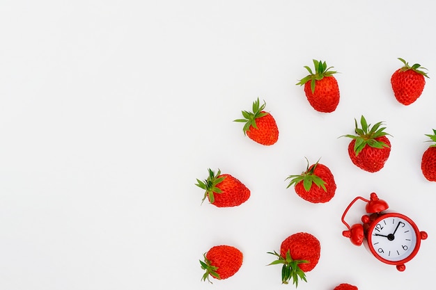 Red alarm clock and flying scattering strawberries berry on white background