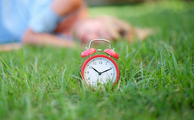 Red alarm clock on grass in background lies woman