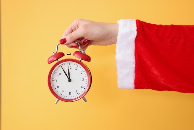 赤い目覚まし時計は、サンタクロースの衣装の新年とクリスマスのお祝いのコンセプトで手を握ります
