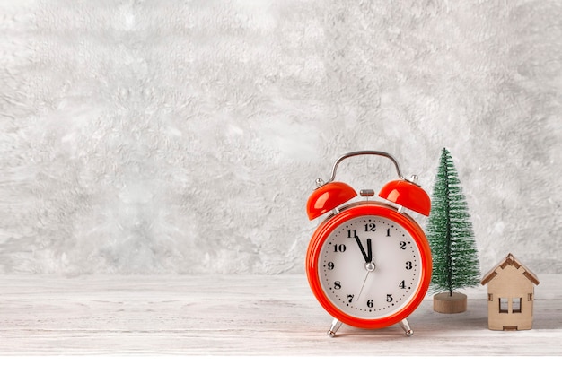 Red alarm clock near a model of a Christmas tree and a wooden house