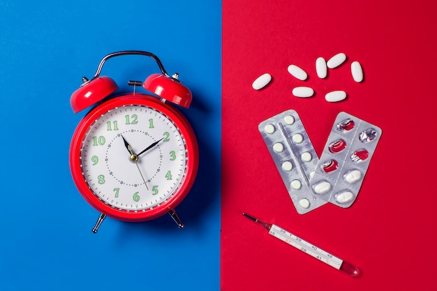 Красный будильник, таблетки и термометр на цвет фона. концепция здравоохранения и медицины