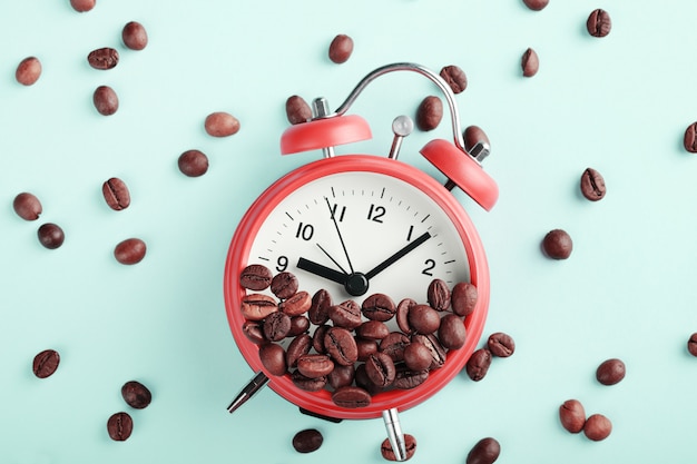 Red alarm clock and roasted coffee beans on blue