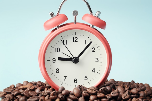 Red alarm clock standing in heap of coffee beans. Concept of morning awakening, beginning of working day