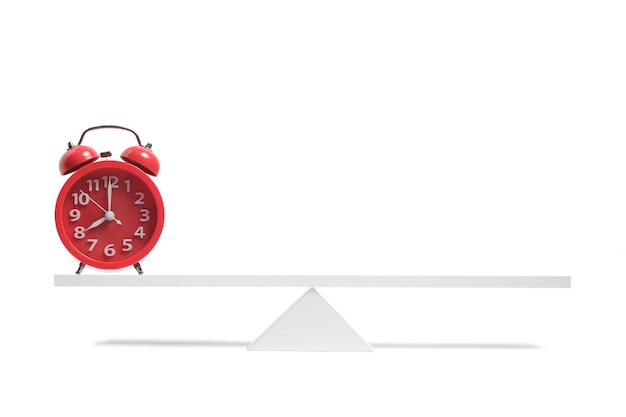 Photo red alarm clock stands on balanced scales on a white background