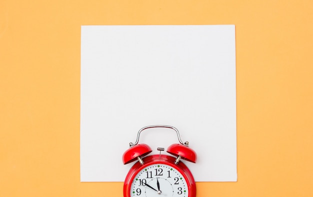 Red alarm clock and white cardboard on yellow