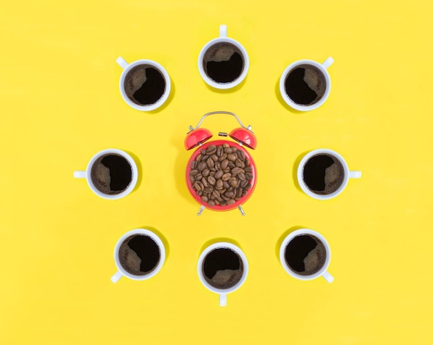 Red alarm clock with coffee beads and coffee cups on the yellow background Top view Copy space