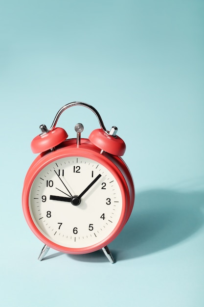 Red alarm clock with shadow on blue background. Seven minutes past nine on the clock