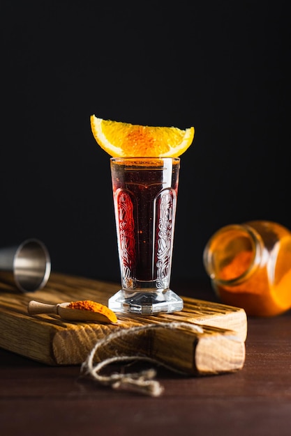 나무 판자에 오렌지 조각과 갈은 붉은 고추를 넣은 유리잔에 붉은 알코올 칵테일